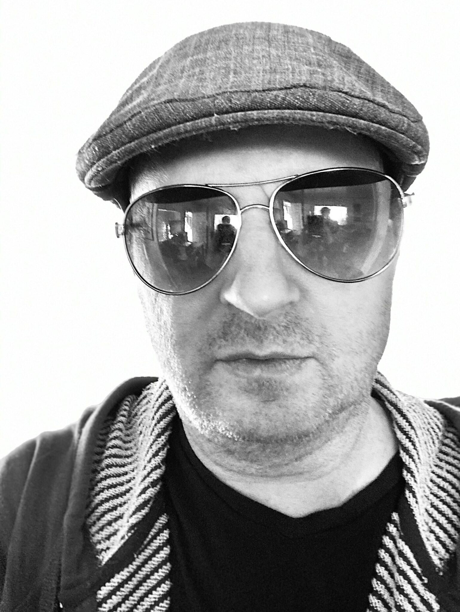 Headshot of an unshaven Isaac Toast in a hoodie and newsboy cap wearing sunglasses